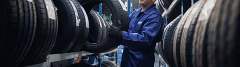 A Point S technician holding a tyre in front of a tyre rack in a tyre shop
