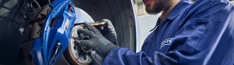 A Point S technician measuring brake pad thickness on a car during a brake check