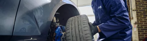A Point S technician holding a wheel to check brake pads and discs on a car in Point S UK centre
