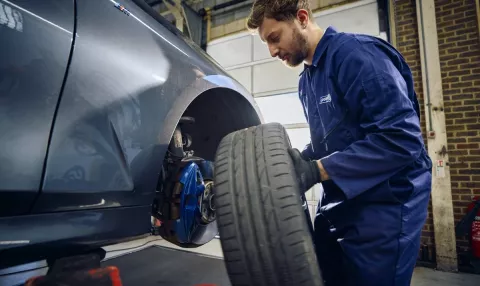 A Point S technician holding a wheel to check brake pads and discs on a car in Point S UK centre