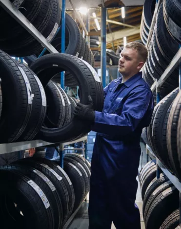 A Point S technician holding a tyre in front of a tyre rack in a tyre shop