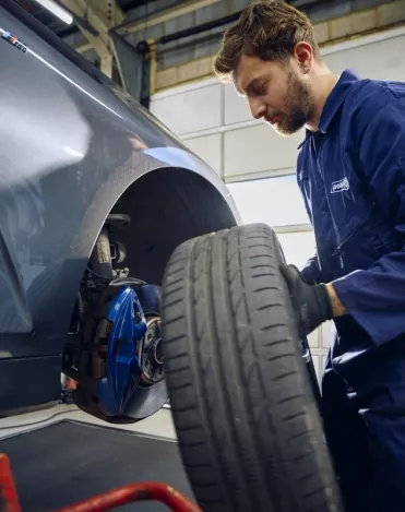 A Point S technician holding a wheel to check brake pads and discs on a car in Point S UK centre
