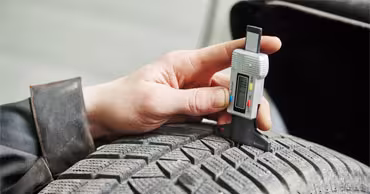 A close up shot of someone checking tyre tread depth with a tyre tread depth gauge