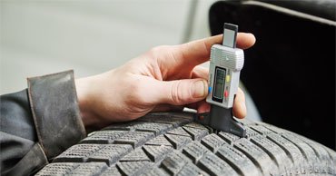 A close up shot of someone checking tyre tread depth with a tyre tread depth gauge