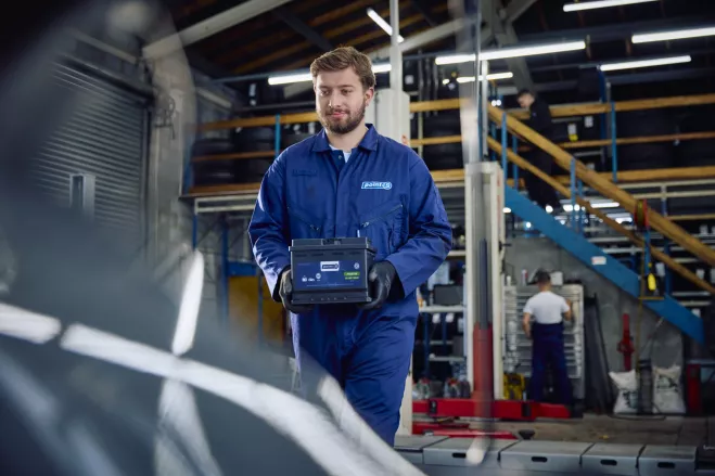 A Point S technician holding a car battery